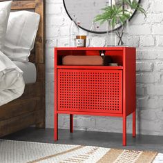 a red cabinet sitting on top of a bed next to a white brick wall with a round mirror above it