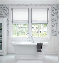 a white bath tub sitting next to two windows in a room with wall paper on the walls