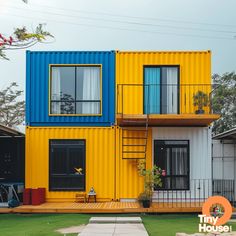 a house made out of shipping containers and painted yellow, blue, and white with stairs leading up to the second floor