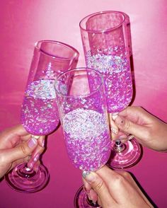 three people are holding up wine glasses with pink liquid in them and glitter on the rims