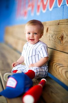 a little boy sitting on top of a wooden bench next to a stuffed baseball bat