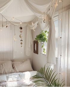 a bed with white sheets and curtains hanging from it's headboard, next to a potted plant