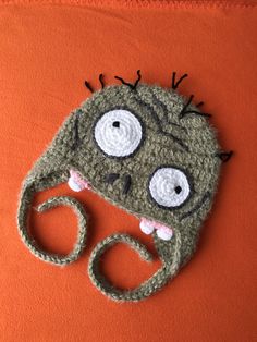 a crocheted monster hat with googly eyes on an orange background