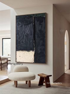 an abstract painting hangs on the wall next to a white chair and footstool