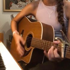 a woman sitting in front of a piano while playing an acoustic guitar with her hands