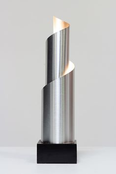 a metal sculpture sitting on top of a black stand next to a white wall and floor