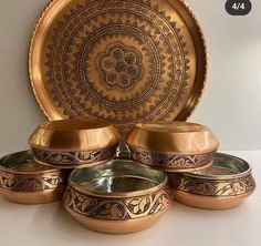 a set of four metal bowls and plates with designs on the bottom one is gold