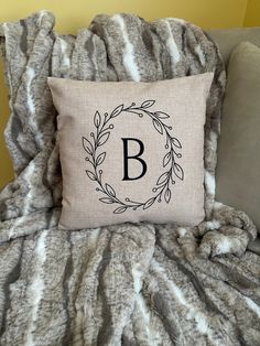 a monogrammed pillow sitting on top of a bed next to a gray blanket