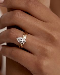 a woman's hand wearing a gold ring with a pear shaped diamond