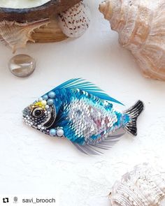 a blue and white fish brooch sitting on top of a table next to seashells