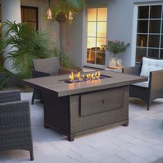 an outdoor fire pit sitting on top of a patio next to wicker chairs and palm trees