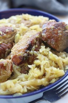 a blue bowl filled with meat and rice on top of a white tablecloth next to a fork