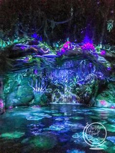 an artificial waterfall in the middle of a pond at night with colorful lights on it