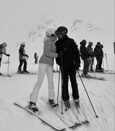 two people standing on skis in the snow with their arms around each other while others stand behind them