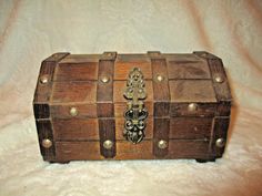 an old wooden box with metal decorations on the lid sitting on a white cloth covered surface