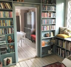 a living room filled with lots of books on top of wooden flooring next to a window