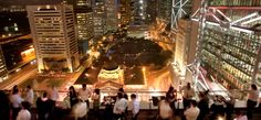 many people are standing on the roof of a tall building at night with city lights in the background