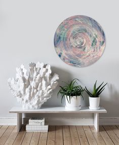 some plants are sitting on a table in front of a wall with a circular painting