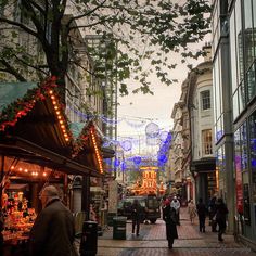 people are walking down the street in front of christmas lights and decorations on display at an outdoor market