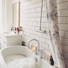 a bath tub sitting next to a white sink in a bathroom under a window with shower curtain