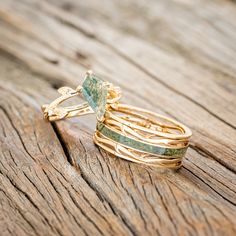 a stack of gold rings with green stones on them sitting on a wooden table top