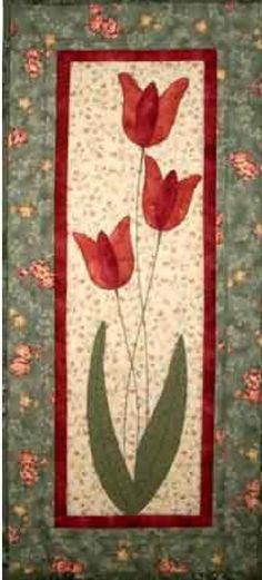 a quilted wall hanging with red flowers and green leaves on the bottom half of it