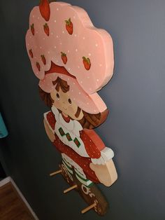 a wooden sculpture of a girl wearing a pink hat and dress with strawberries on it