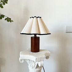 a lamp is sitting on top of a white pedestal next to a plant in a vase