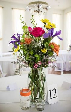 a vase filled with lots of colorful flowers on top of a white table cloth covered table