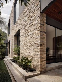 a modern house with stone walls and plants in the front yard, surrounded by lush greenery