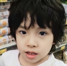 a young boy with black hair and blue eyes in a grocery store looking at the camera