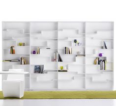 a white book shelf filled with lots of books on top of each other in front of a wall