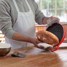 a man holding a loaf of bread on top of a wooden table in front of an oven