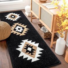 a black rug with white and brown designs on the floor next to a plant in a vase