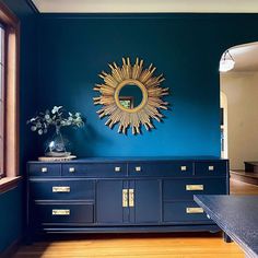 a room with blue walls and wooden floors has a gold sun mirror on the wall