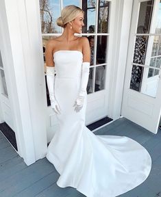 a woman standing in front of a door wearing a white wedding dress and long gloves