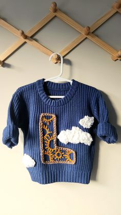 a blue sweater with clouds on it hanging from a wooden hanger and some clothes pegs