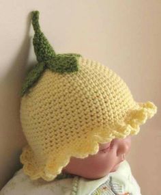 a crocheted lemon hat on top of a doll's head, against a wall