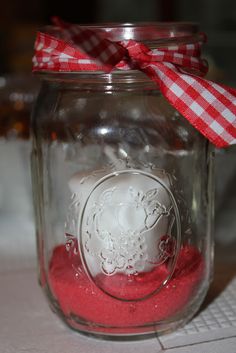 a glass jar filled with red sand next to a white and red checkered ribbon