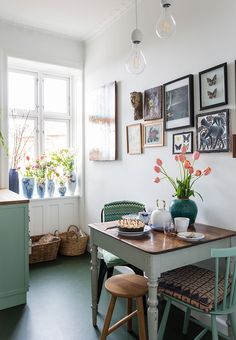 a dining room table with two chairs and pictures on the wall above it in front of a window