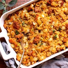 a casserole dish filled with stuffing on top of a wooden table next to a spoon