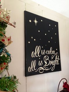 a black and white sign that says all is calm, all is bright next to a christmas tree