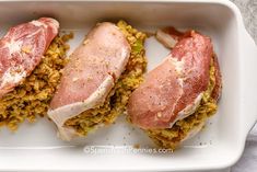 two pieces of meat sitting on top of some food in a white dish with yellow and green toppings