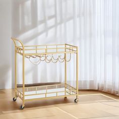 a gold serving cart with two trays on wheels in front of a white wall