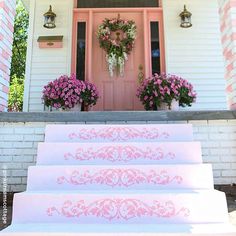 steps leading up to the front door of a white house with pink flowers and wreaths