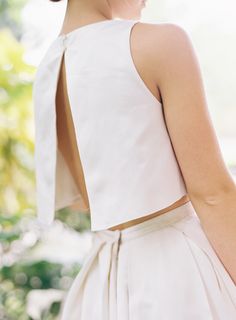 the back of a woman's white dress with an open neck and bow at the waist