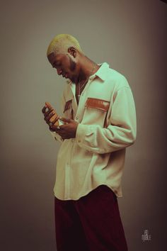 a man in a white shirt and red pants looking at his cell phone while standing against a gray background