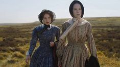 two women dressed in period clothing walking through an open field