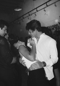 black and white photograph of two men hugging each other in a dance hall, one man is holding the woman's neck