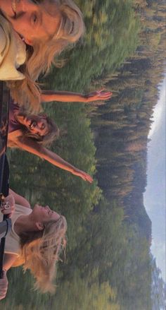 two women standing next to each other in front of a body of water with trees